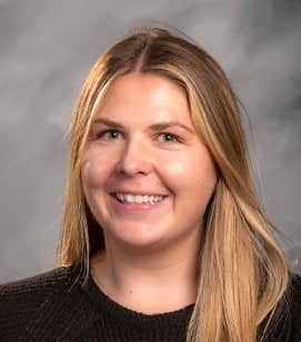 Headshot of a Caucasian woman smiling. She has long blonde hair and is wearing a black shirt